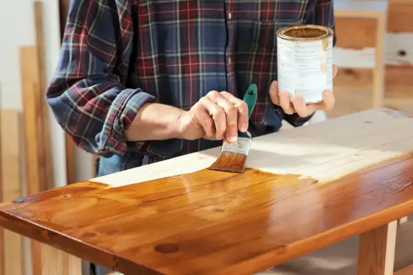 Mano che applica mordente su legno con pennello. Il mordente significato è dare colore e profondità al legno.