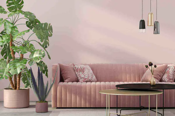 Divano rosa cipria su muri color tortora rosato, con piante verdi e tavolini dorati.