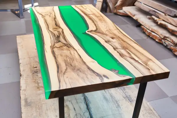 Tavolo con resina verde brillante tra venature di legno. La differenza tra levigatura e lucidatura è evidente nella finitura liscia e riflettente.