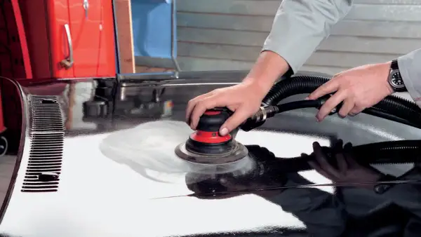 Mani esperte utilizzano una levigatrice per stuccare auto, preparando la carrozzeria per una finitura impeccabile.