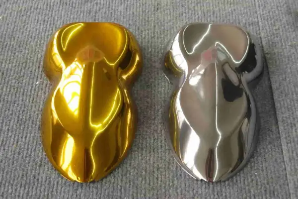 Due campioni di vernice, uno oro brillante e l'altro con un effetto cromo colore metallico, riflettono la luce su una superficie grigia.
