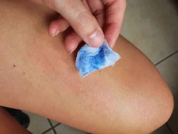 Mano che pulisce la pelle con un dischetto di cotone blu, mostrando come togliere la vernice dalla pelle in modo efficace.