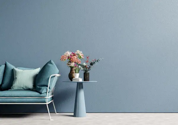Divano blu petrolio con cuscini, tavolino azzurro con vasi di fiori. La materia e i colori creano un'atmosfera rilassante.