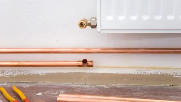 Installazione di tubi in rame per il riscaldamento, con un raccordo a T e una connessione al radiatore. La coibentazione dei tubi riscaldamento è fondamentale per l'efficienza.