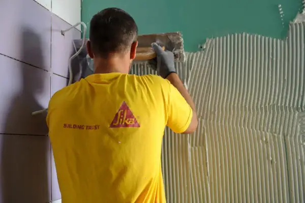 Operaio con maglia gialla Sika applica colla per incollare piastrelle su piastrelle parete.