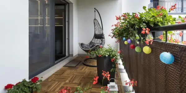 Un balcone accogliente con pavimento in legno, una sedia sospesa e fiori rossi. Un'idea per rivestire pavimento balcone fai da te.
