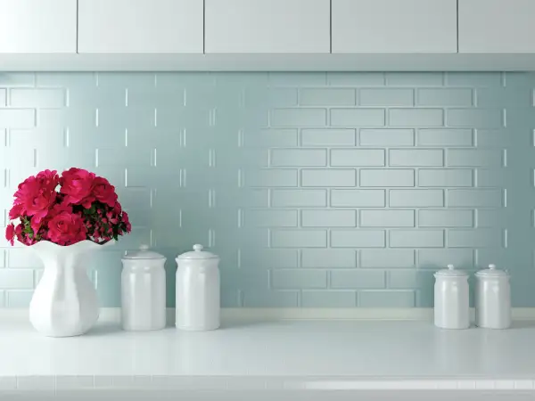 Un vaso bianco con fiori rossi e barattoli su un piano di lavoro. Un'idea per come verniciare le piastrelle della cucina con un tocco di colore.