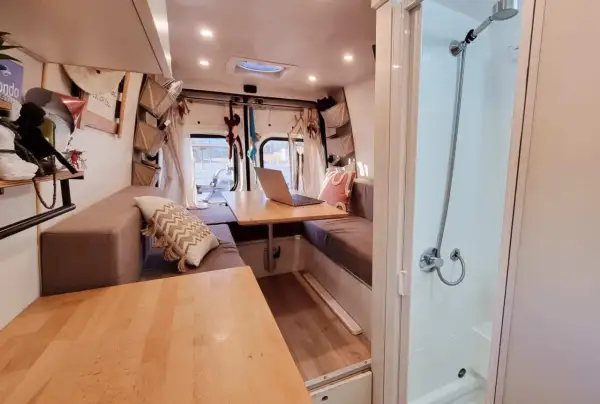 Interno camper con divanetti, tavolo e un box doccia in legno fai da te.