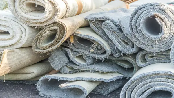 Rotoli di moquette accatastati, pronti per essere rimossi. Si vedono i bordi sfilacciati e i diversi strati dei tappeti.