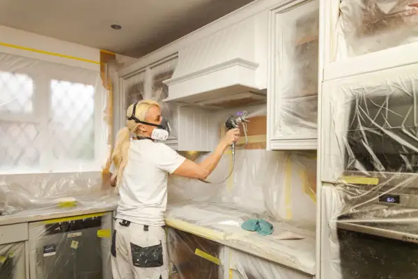 Donna con maschera protettiva effettua un cambio colore ai mobili della cucina con uno spruzzatore di vernice.