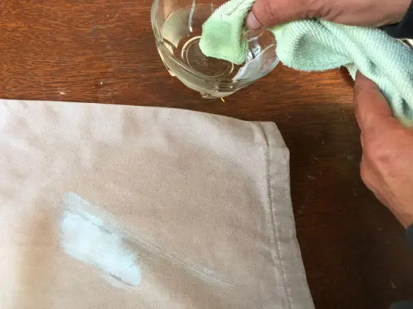Mani che tamponano una macchia di vernice secca su un tessuto beige con un panno umido, per togliere macchie di vernice secca dai vestiti.