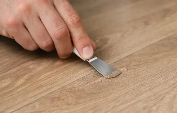 Mano che applica stucco per la riparazione parquet su una fessura del legno.