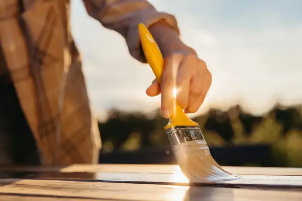Mano che stende vernici poliuretaniche bicomponenti su un tavolo di legno al tramonto, per una finitura protettiva e duratura.