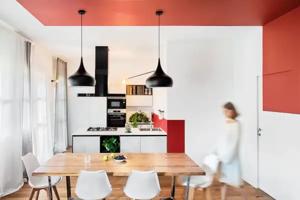 Un soggiorno moderno con soffitti colorati, un tavolo in legno, sedie bianche e una cucina a vista.