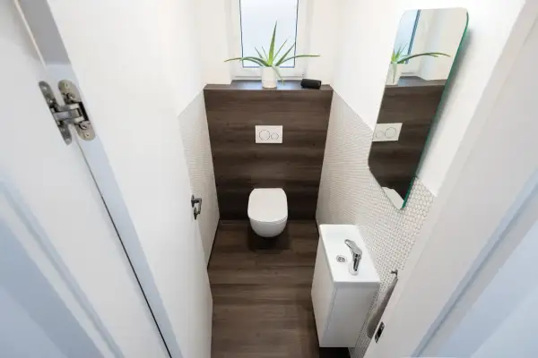 Bagno piccolo con WC sospeso, lavandino bianco e specchio asimmetrico. Un esempio di come piastrellare un bagno piccolo con stile.