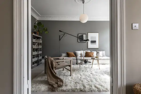 Soggiorno moderno con pareti color grigio piombo, divano modulare, poltrona in legno e un soffice tappeto bianco.
