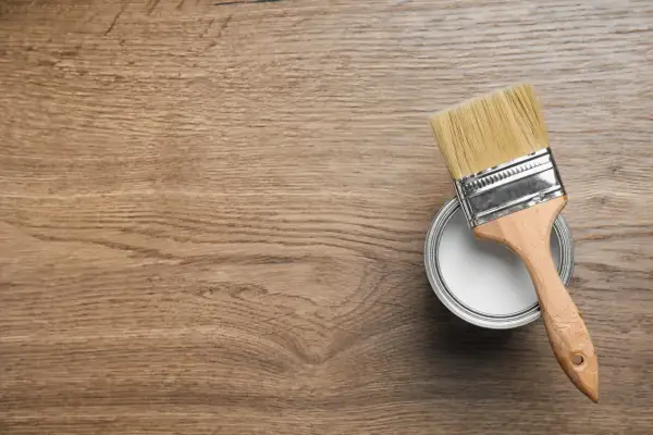 Pennello e barattolo di vernice bianca pronti per colorare legno su una superficie di legno grezzo.