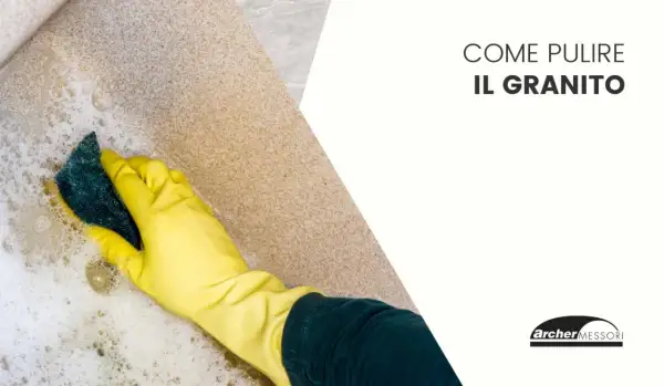 Mano con guanto giallo pulisce una superficie in granito con una spugna e schiuma.